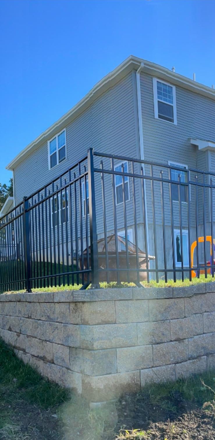 Black aluminum fence installed above a block retaining wall beside a house