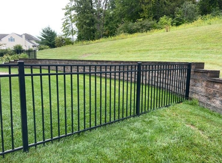 Black aluminum fence installed along a residential yard and retaining wall